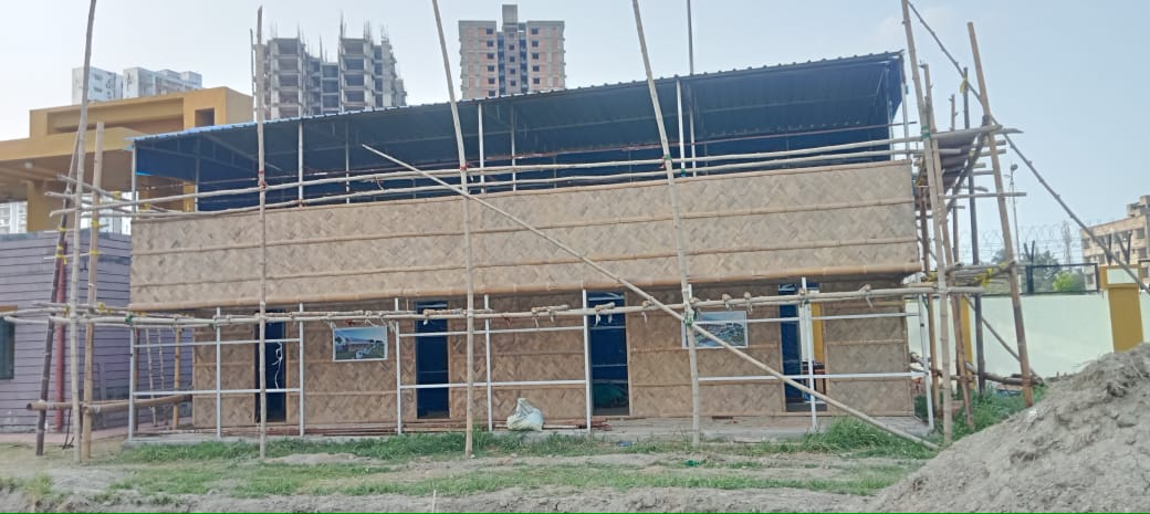 The habitat mid-construction — scaffolding surrounds the two-story structure, woven panels on both floors, bare ground