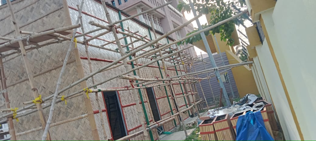 Bamboo scaffolding around the building, woven panels installed on both floors, red window frames visible