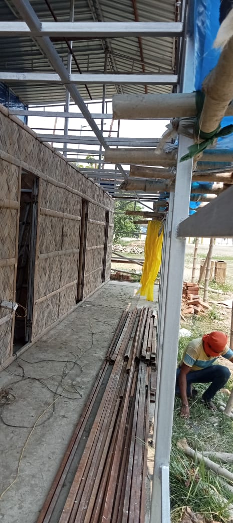 Upper floor steel frame still exposed while ground floor bamboo cladding nears completion, worker visible