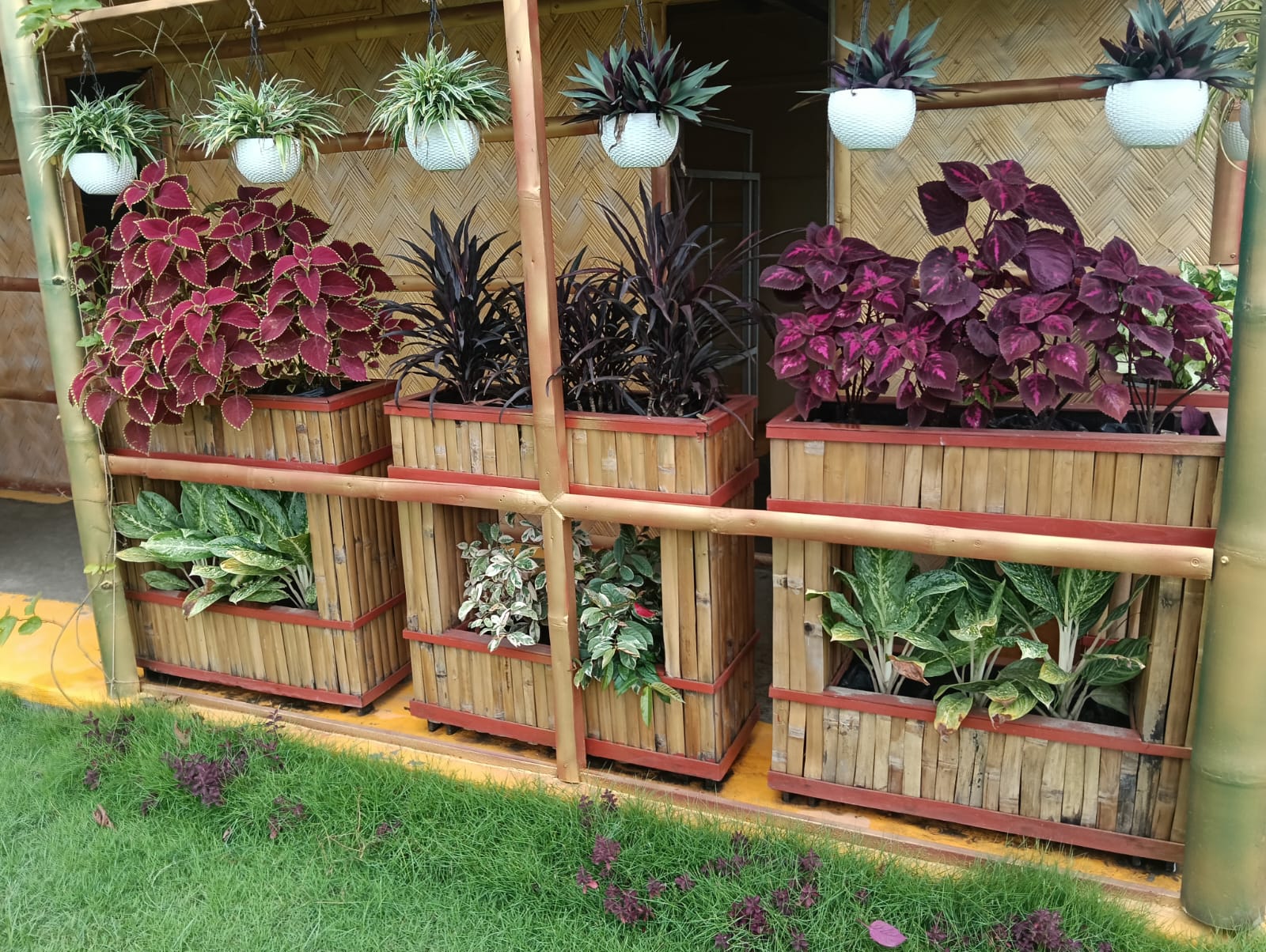 Close-up of the integrated planter system — coleus in deep reds and purples, ornamental foliage in bamboo planter boxes with hanging planters above