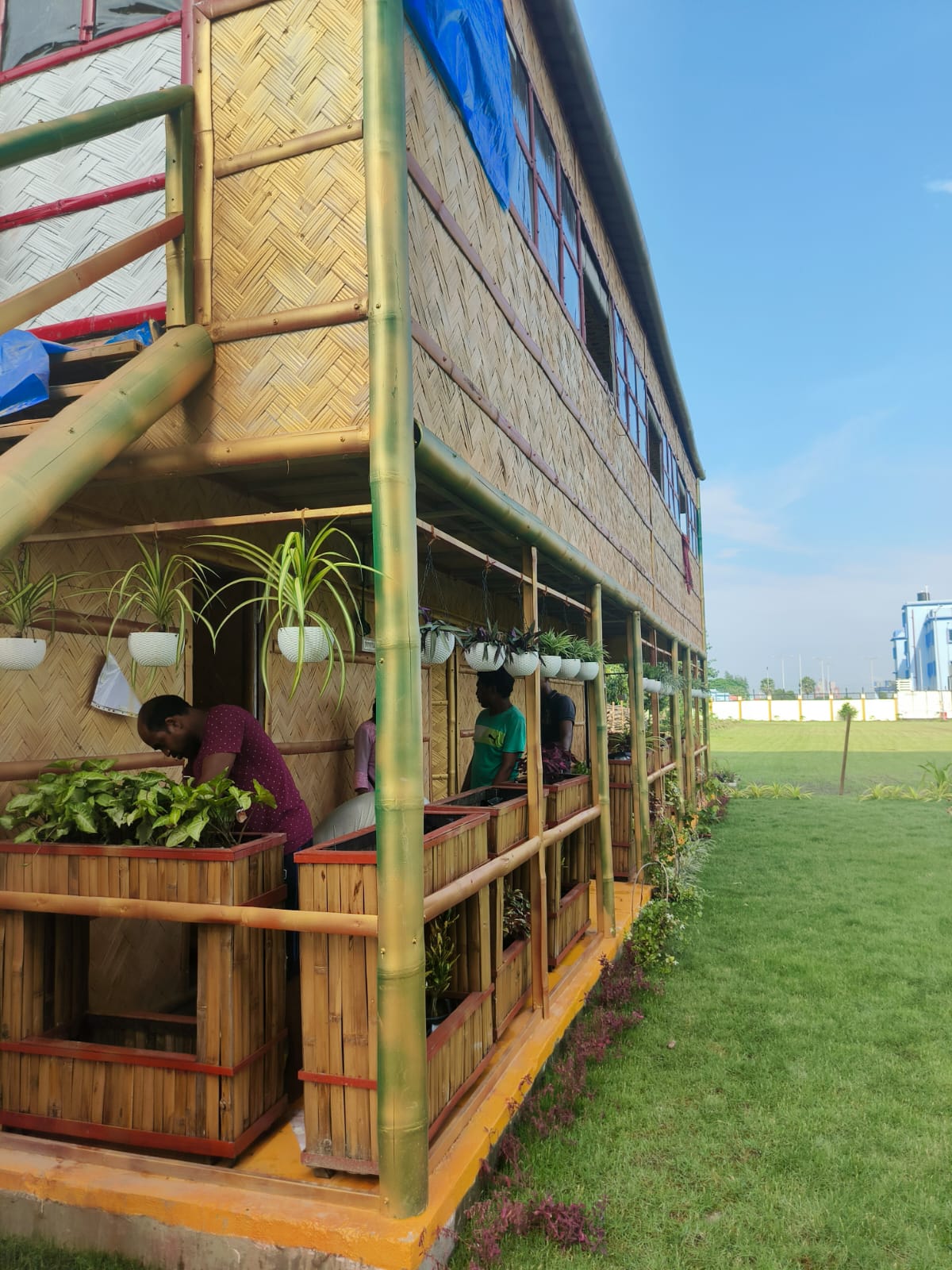 Side view showing thick Ganga Bamboo structural poles supporting two stories, with woven bamboo panels and integrated planter boxes