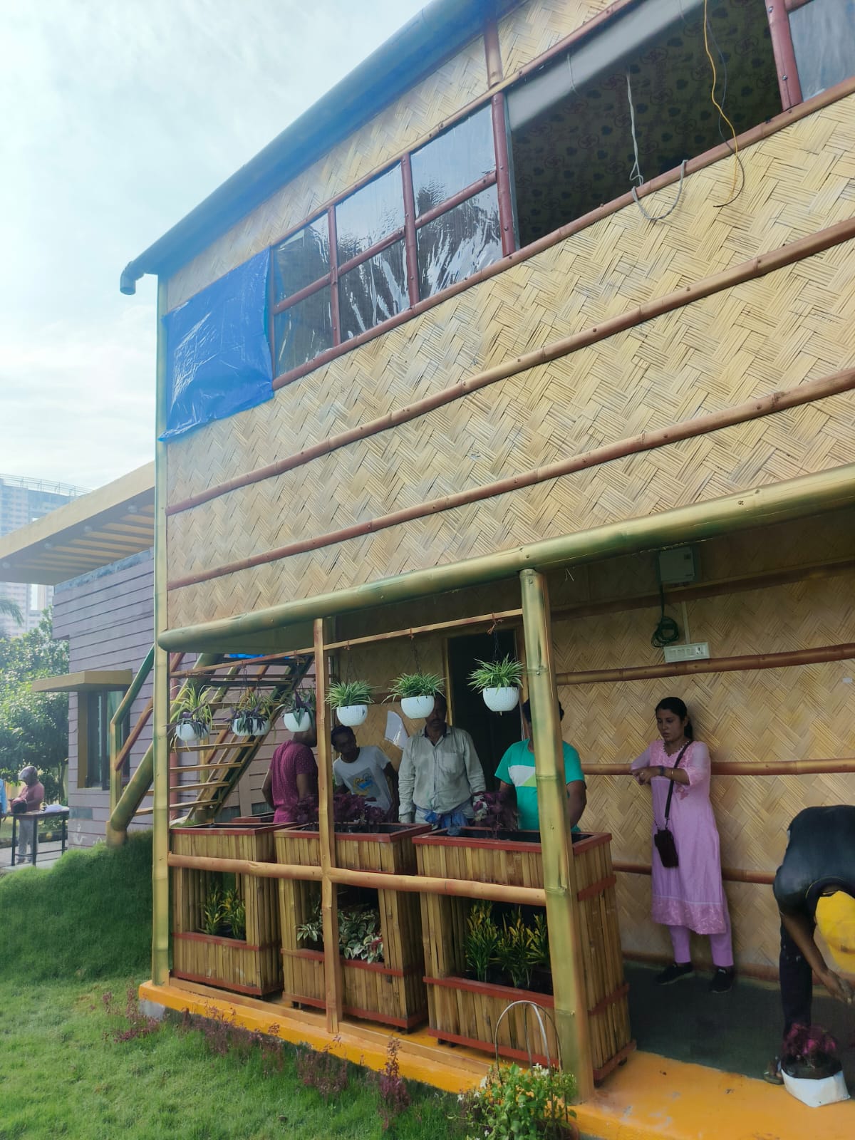 Corner view showing visitors exploring the ground floor, bamboo ladder staircase to the upper level