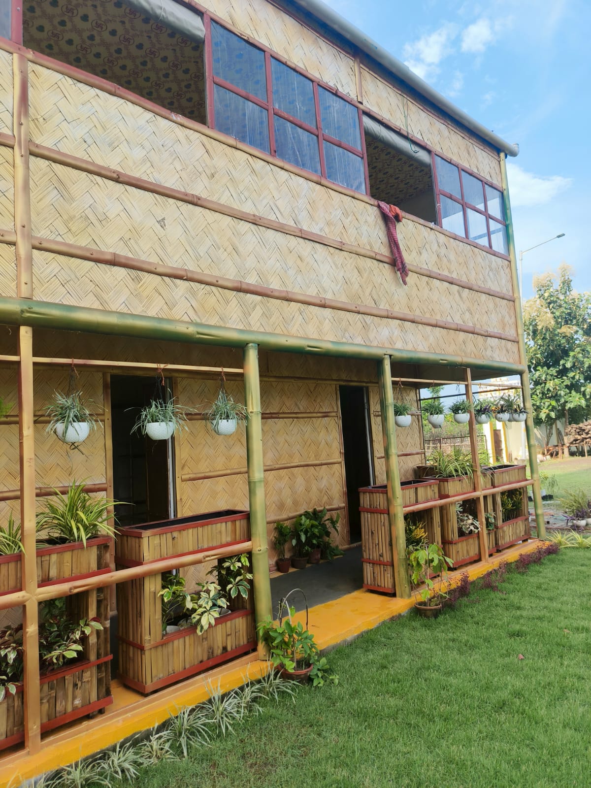 The completed Biophilic Habitat — full facade view showing woven bamboo walls, red window frames, and integrated planter system along the ground floor